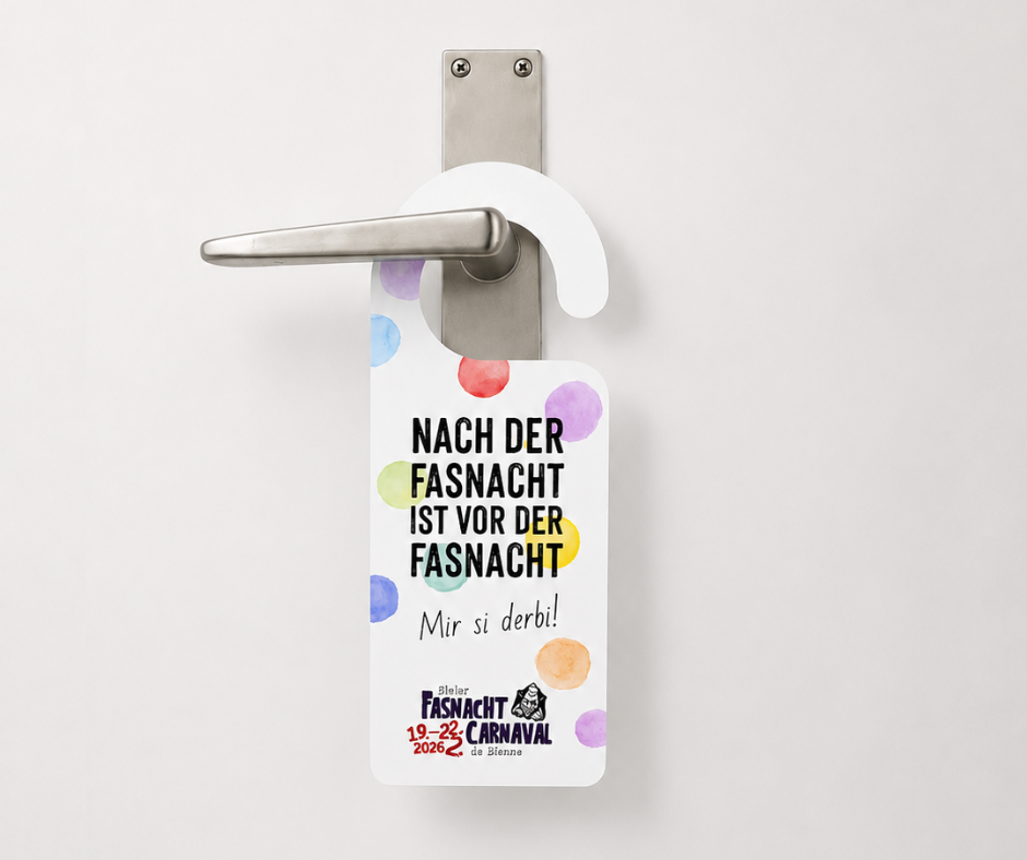 Türhänger mit farbigen Aquarellpunkten hängt an einer modernen Edelstahl-Türklinke vor einem schlichten, hellen Studiohintergrund. Die Gestaltung trägt den Slogan «Nach der Fasnacht ist vor der Fasnacht» sowie den Zusatz «Mir si derbi!» und verweist auf die Bieler Fasnacht 2026. Das reduzierte Design mit viel Freiraum setzt den individuell gestalteten Türhänger hochwertig und aufmerksamkeitsstark in Szene.